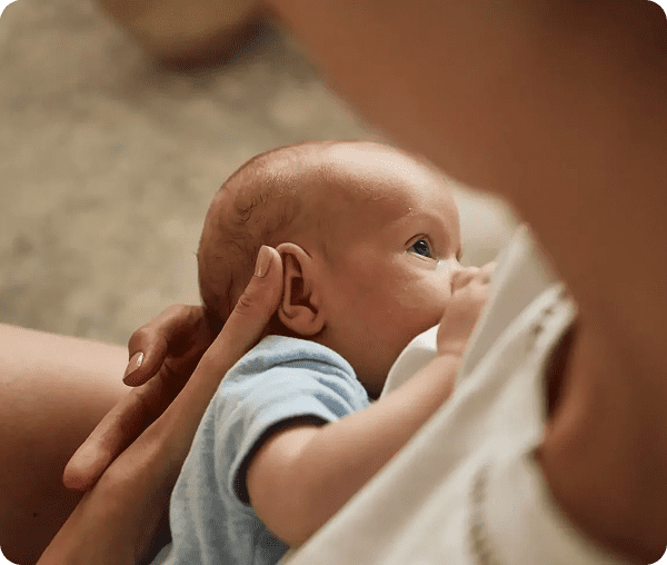 A baby breastfeeding while being gently touched on the head.